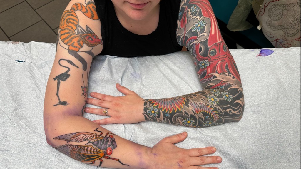 Anna's arms crossed on a table displaying their arm tattoos